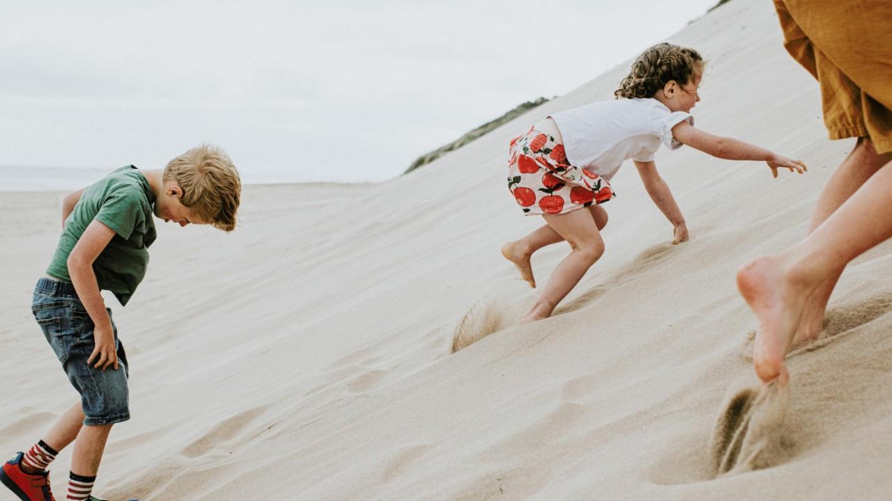 三个孩子在陡峭的沙丘上玩耍, 这需要大量的努力，因为柔软的沙子在他们的脚和手下面